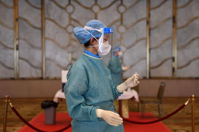 © Bloomberg. A worker in a protective suit holds a sample from a guest to test for the COVID-19 novel coronavirus in Beijing on September 30, 2020, ahead of a reception being held by Chinese leaders on the eve of China's National Day.  Photographer: Greg Baker/AFP via Getty Images