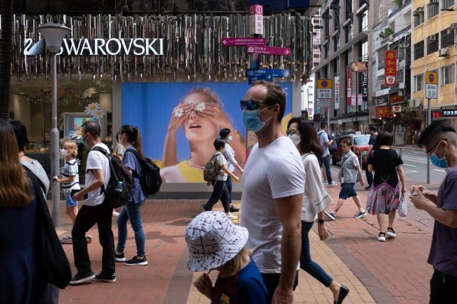 © Bloomberg. Pedestrians wearing protective masks walk past a Swarovski AG store in the Causeway Bay district in Hong Kong, China, on Friday, May 1, 2020. The outbreak of Covid-19 and the government's subsequent social-distancing restrictions have, over the past few months, largely suppressed pro-democracy protests that rocked the Asian financial hub last year. But as virus cases ease, activists have begun organizing new demonstrations, defying the measures. Photographer: Roy Liu/Bloomberg