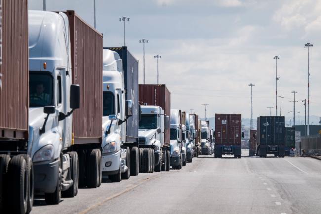 © Bloomberg. Trucks wait in line to enter the Port of Oakland in Oakland, California, U.S., on Thursday, March 19, 2020. The spread of the coronavirus pandemic is scrambling supply chains in everything from crude oil to copper and foodstuffs, with many countries reporting a shortage of containers. Photographer: David Paul Morris/Bloomberg