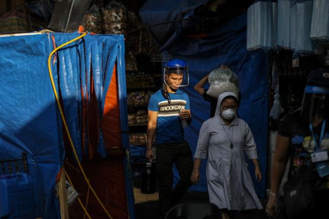 © Bloomberg. A pedestrian wearing a face shield walks behind a nun wearing a mask at a market during a partial lockdown imposed due to the coronavirus in Quezon City, Metro Manila, the Philippines, on Wednesday, May 20, 2020. The Philippines is considering downsizing lockdowns to villages from regions, as it balances further reopening its economy with stemming the virus outbreak Photographer: Veejay Villafranca/Bloomberg