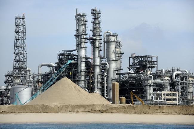 © Bloomberg. A chemical refinery stands behind a stockpile of sand to be used as landfill on Jurong Island in Singapore, on Thursday, March 1, 2012. Singapore is Asia's largest oil-trading and storage center. Photographer: Munshi Ahmed/Bloomberg 