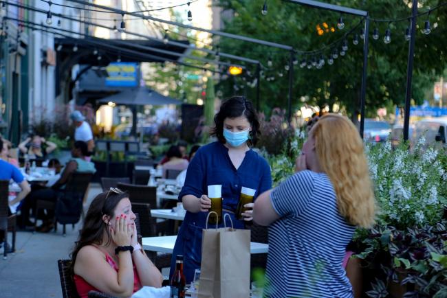 © Bloomberg. A waiter wearing a protective mask delivers checks to patrons at the outdoor seating area of a restaurant in Chicago, Illinois, U.S., on Friday, July 24, 2020. Chicago is reinstating restrictions “in certain high-risk environments” for the first time since reopening its economy last month to prevent an uptick in Covid-19 cases from turning into a resurgence. Photographer: Olivia Obineme/Bloomberg