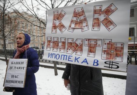 © Reuters/Maxim Zmeyev. Protesters hold placards during a picket in central Moscow, Dec. 12, 2014. According to local media, the people, who took mortgages in foreign currencies, now face larger risks due to the weakening of the rouble. The placards read, 'Banks make us beggars', 'How to live. Mortgages in dollars'.