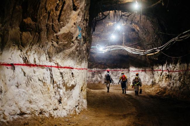 © Bloomberg. Miners walk through an underground tunnel at a gold mine in South Africa.