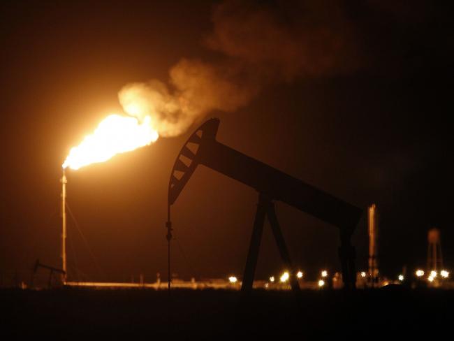 © Bloomberg. The silhouette of an electric oil pump jack is seen near a flare at night in the oil fields surrounding Midland, Texas. Photographer: Luke Sharrett/Bloomberg