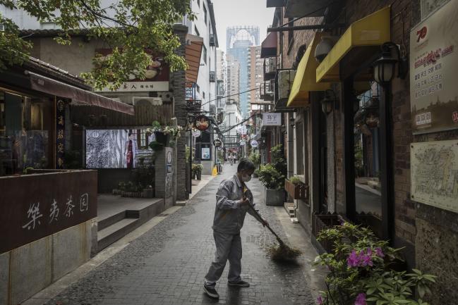 © Bloomberg. A man wearing a protective mask sweeps a lane in front of stores in the Tianzifang retail precinct in Shanghai, China, on Monday, April 20, 2020. Chinese banks lowered borrowing costs and the government promised to sell another 1 trillion yuan ($141.3 billion) in bonds to pay for stimulus spending after the economy had its first contraction in decades due to the coronavirus outbreak.