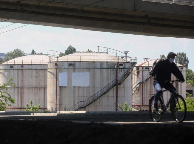 © Bloomberg. A cyclist wearing a protective face mask rides past oil storage silos at an oil and gas storage facility, operated by Gazprom Neft PJSC, in Belgrade, Serbia, on Tuesday, April 28, 2020. Crude whipsawed near $11 a barrel after a major index tracked by billions of dollars in funds bailed out of near-term contracts for fear prices may turn negative again. Photographer: Oliver Bunic/Bloomberg