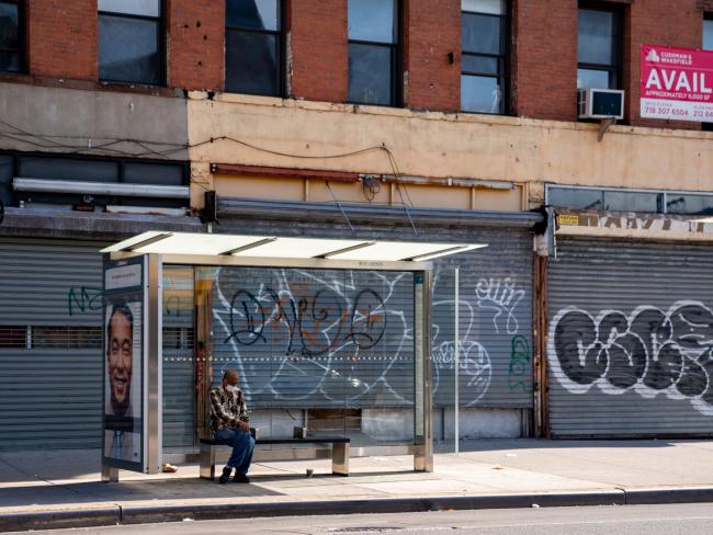 © Bloomberg. A person sits at a bus stop next to closed businesses in Brooklyn, New York on June 17. Photographer: David Dee Delgado/Bloomberg