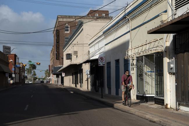 © Bloomberg. A person rides a bicycle near an empty street in downtown Brownsville, Texas, U.S., on Thursday, July 30, 2020. The Rio Grande Valley, a four-county region that stretches across Texas's southernmost tip, remains one of America's most afflicted areas, with the highest hospitalization rates, deaths at more than twice the state average, overwhelmed hospitals and refrigerated trucks serving as back-up morgues. Photographer: Callaghan O'Hare/Bloomberg