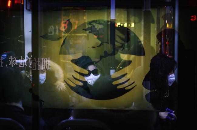 © Bloomberg. BEIJING, CHINA - MARCH 02: Seen through the reflection of an advertisement, Chinese office workers wear protective masks as they ride on a public bus after leaving work on March 2, 2020 in Beijing, China. The number of cases of the deadly new coronavirus COVID-19 being treated in China dropped to below 33,000 in mainland China Monday, in what the World Health Organization (WHO) declared a global public health emergency last month. China continued to lock down the city of Wuhan, the epicentre of the virus, in an effort to contain the spread of the pneumonia-like disease. Officials in Beijing have put in place a mandatory 14 day quarantine for all people returning to the capital from other places in China. The number of those who have died from the virus in China climbed to over 2900 on Monday, mostly in Hubei province, and cases have been reported in other countries including the United States, Canada, Australia, Japan, South Korea, India, Iran, Italy, the United Kingdom, Germany, France and several others. The World Health Organization has warned all governments to be on alert and raised concerns over a possible pandemic. Some countries, including the United States, have put restrictions on Chinese travellers entering and advised their citizens against travel to China.(Photo by Kevin Frayer/Getty Images)