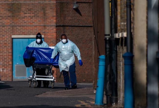 © Bloomberg. LONDON, ENGLAND - APRIL 16: Hospital workers wheel a concealment trolley, typically used for transporting bodies, to the mortuary at Lewisham Hospital on April 16, 2020 in London, UK. The Lewisham and Greenwich NHS Trust, which runs Lewisham Hospital and Queen Elizabeth Hospital in Greenwich, reported 14 deaths from Covid-19 occurring between March 27 and April 12. The hospital recently installed refrigerated containers in its car park. The Coronavirus (COVID-19) pandemic has spread to many countries across the world, claiming over 130,000 lives and infecting over 2 million people. (Photo by Chris J Ratcliffe/Getty Images)