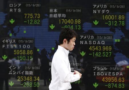 © Reuters/Issei Kato. A passerby walks past an electric screen displaying stock market indices of various countries outside at a brokerage in Tokyo, Japan, Sept. 29, 2015.