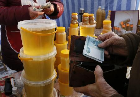 © Reuters/Ilya Naymushin. A customer (R) holds a 1,000 Russian Rouble banknote as she comes to buy honey at an open-air food fair in Krasnoyarsk, Siberia, Jan. 14, 2015. The Russian rouble weakened on Wednesday, tracking lower oil prices, but was lifted by a Finance Ministry plan to convert .6 billion (5 billion pounds) in forex reserves.