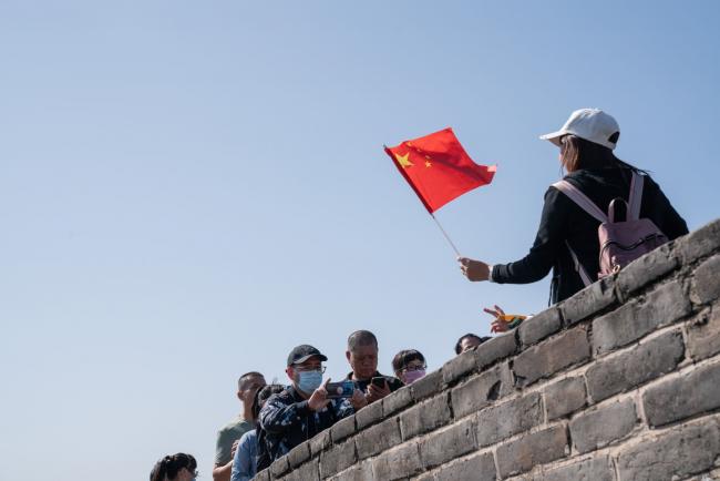 © Bloomberg. A visitor holds a Chinese flag while posing for a photograph at the Badaling section of the Great Wall in Beijing, China, on Thursday, Oct. 1, 2020. China's so-called Golden Week holiday this year starts with the Mid-Autumn Festival and National Day on Thursday and runs to Oct. 8. Photographer: Yan Cong/Bloomberg