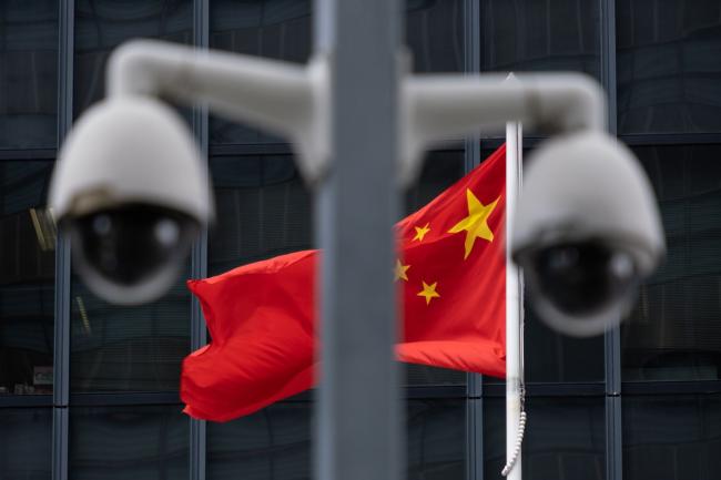 © Bloomberg. The flag of China is flown behind a pair of surveillance cameras outside the Central Government Offices in Hong Kong, China, on Tuesday, July 7, 2020. Hong Kong leader Carrie Lam defended national security legislation imposed on the city by China last week, hours after her government asserted broad new police powers, including warrant-less searches, online surveillance and property seizures. Photographer: Roy Liu/Bloomberg