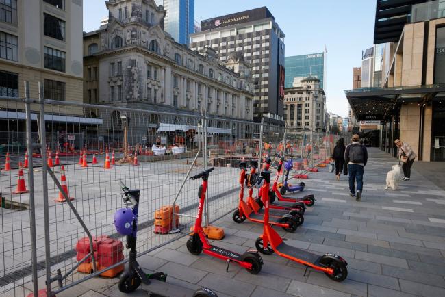 © Bloomberg. Pedestrians walk past scooters on a street undergoing construction works in Auckland, New Zealand, on Wednesday, Sept. 16, 2020. New Zealand’s economy will endure a shallower recession than previously expected but the coronavirus pandemic will have a longer impact on the country’s finances, according to government projections. Photographer: Brendon O'Hagan/Bloomberg