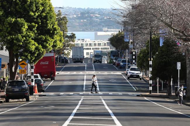 © Bloomberg. A woman crosses an empty street in Auckland as the city returns to lockdown on Aug. 13.