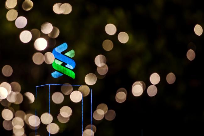 © Bloomberg. Signage is illuminated atop the Standard Chartered Bank building at night in Hong Kong, China, on Thursday, July 25, 2019. Standard Chartered is scheduled to release interim earnings results on Aug. 1. Photographer: Paul Yeung/Bloomberg