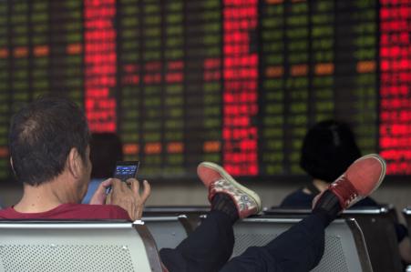 © Johannes Eisele/AFP/Getty Images. The Shanghai Stock Exchange is proposing a new rule that would halt trading on China's three mainland exchanges if the benchmark CSI300 index moves 5 percent or 7 percent in either direction in one trading day. Pictured: An investor checks his smartphone as a digital board shows stock market movements at a brokerage house in Shanghai, on Sept. 1, 2015.