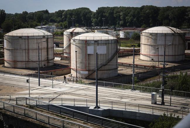 © Bloomberg. A pedestrian passes oil storage silos at an oil and gas storage facility, operated by Gazprom Neft PJSC, in Belgrade, Serbia, on Tuesday, April 28, 2020. Crude whipsawed near $11 a barrel after a major index tracked by billions of dollars in funds bailed out of near-term contracts for fear prices may turn negative again. Photographer: Oliver Bunic/Bloomberg