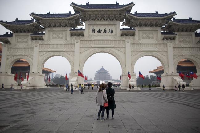 © Bloomberg. Visitors stand at Liberty Square as the Chiang Kai-shek Memorial Hall stands in the background in Taipei, Taiwan, on Sunday, Dec. 31, 2017. Taiwan’s currency rose 18 percent in 2017, its best annual performance in three decades, largely the result of a weakening greenback. Photographer: Brent Lewin/Bloomberg