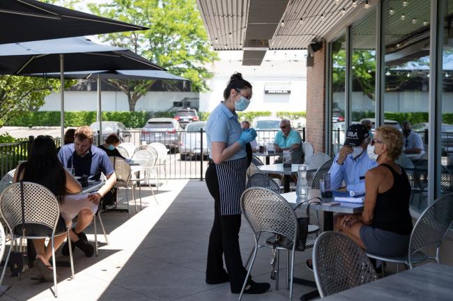 © Bloomberg. A server wearing a protective mask assists customers in the outside seating area of a restaurant. Photographer: Emily Elconin/Bloomberg