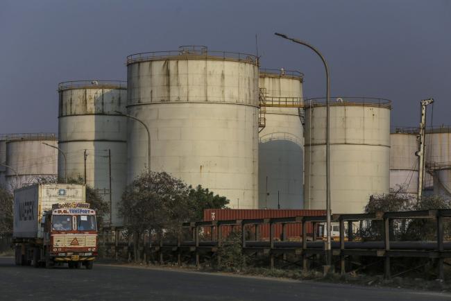 © Bloomberg. A container truck travels past oil storage tanks at Jawaharlal Nehru Port, operated by Jawaharlal Nehru Port Trust (JNPT), in Navi Mumbai, Maharashtra, India, on Monday, March 30, 2020. As billions of people stay home in the the world's major economic centers, consumption of everything from transport fuel to petrochemical feedstocks is in freefall. Refiners that have already been filling up their storage tanks with unsold products now have little choice but to partially shut down their plants. Photographer: Dhiraj Singh/Bloomberg