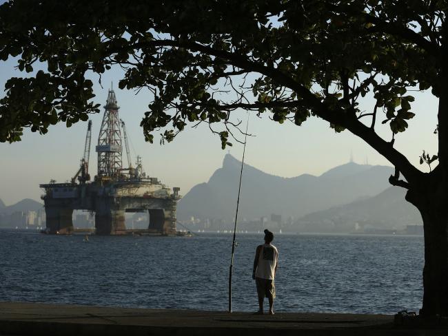 © Bloomberg. A man fishes in Guanabara Bay while an oil drilling platform floats in the background near Niteroi, Brazil. Photographer: Dado Galdieri/Bloomberg