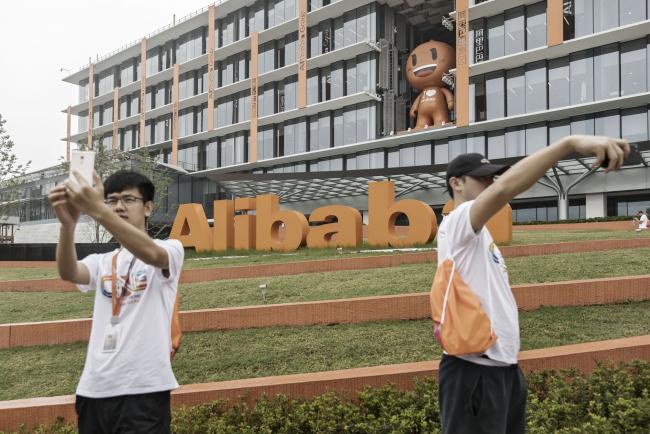 © Bloomberg. Employees and visitors take selfie photographs in front of Alibaba Group Holding Ltd. signage at the company's headquarters in Hangzhou, China, on Friday, Sept. 8, 2017. After conquering grocery deliveries, Alibaba is setting its sights on a new part of China’s $4 trillion retail sector: department stores. Photographer: Qilai Shen/Bloomberg