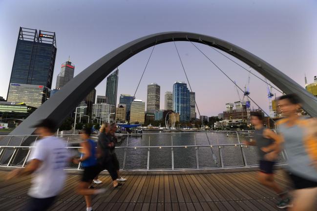 © Bloomberg. Joggers run past pedestrians on the Horseshoe Bridge in the Elizabeth Quay area of Perth, Australia, on Wednesday, April 11, 2018. Australia is scheduled to release employment figures on April 19. Photographer: Sergio Dionisio/Bloomberg