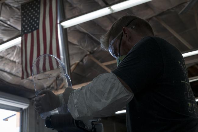 © Bloomberg. A worker wearing a protective mask, gloves, and glasses sands an edge of a face shield at Mask & Shield, a division of Monster City Studios, in Fresno, California, U.S., on Wednesday, May 27, 2020. Monster City Studios, a company that normally makes amusement park and movie props, has pivoted to manufacturing MCS face shields with forehead protection. Photographer: David Paul Morris/Bloomberg