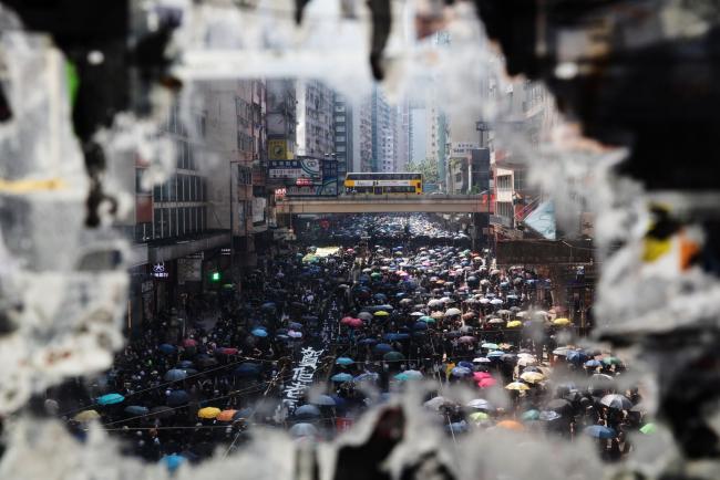 © Bloomberg. Demonstrators marching along Hennessy Road are seen through a ripped poster displayed on a bridge during a protest in the Causeway Bay district of Hong Kong, China, on Tuesday, Oct. 1, 2019. Police shot tear gas volleys at protesters as simultaneous rallies raged across Hong Kong, including a march through the city center, hours after celebrations for a holiday marking 70 years of Communist rule in China began in Beijing. Photographer: Kyle Lam/Bloomberg