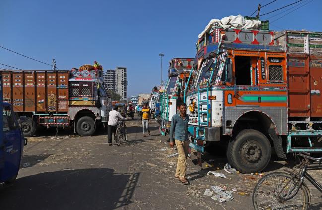 © Bloomberg. People walk past trucks during a lockdown imposed due to the coronavirus in New Delhi, India, on Saturday, March 28, 2020. Indian Prime Minister Narendra Modi ordered the unprecedented move this week in a bid to replicate China’s relative success containing the coronavirus outbreak. But he faces perhaps more obstacles than his neighbor President Xi Jinping, who leveraged the Communist Party’s centralized control to isolate some 60 million people in the province of Hubei, where Covid-19 first emerged.