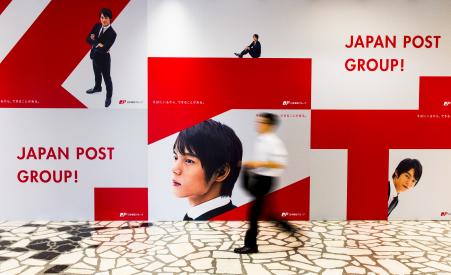 © Reuters/Thomas Peter. Japan Post Holdings and its unit companies will be publicly listed in November, according to Thursday reports. In this photo, a man walks past an advertising poster in the headquarters of Japan Post in Tokyo on June 26, 2015.