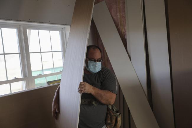 © Bloomberg. A contractor wearing a protective mask moves pieces of sheet rock while working at a home under construction. Photographer: Angus Mordant/Bloomberg