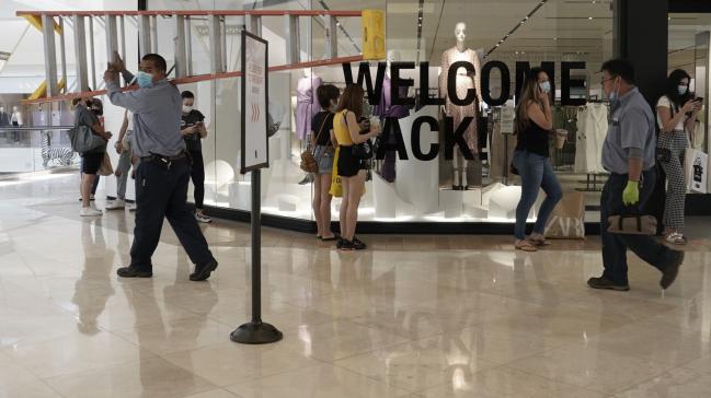 © Bloomberg. Workers walk past shoppers waiting to enter a store inside the South Coast Plaza shopping mall in Costa Mesa, California on June 15, 2020. Photographer: Bing Guan/Bloomberg