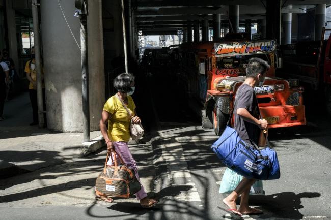 © Bloomberg. Pedestrians wearing protective masks walk with luggage in Quezon City, Metro Manila, the Philippines, on Saturday, March 14, 2020. President Rodrigo Duterte said he would place some 12 million people in the Manila area on lockdown and largely suspend government work for a month in an effort to stop the coronavirus from spreading. Photographer: Veejay Villafranca/Bloomberg