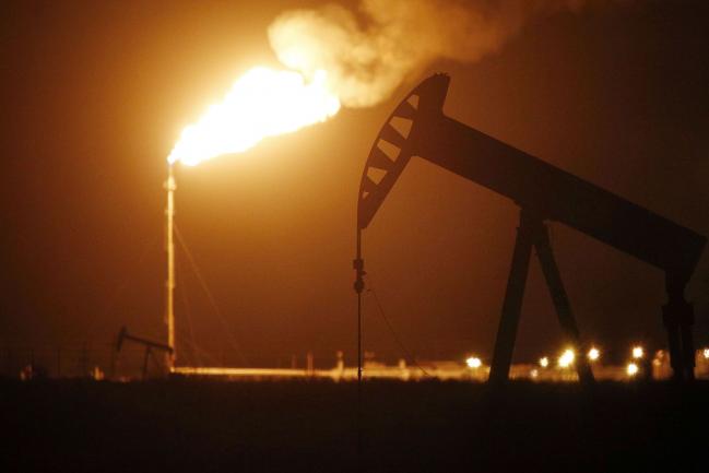 © Bloomberg. The silhouette of an electric oil pump jack is seen near a flare at night in the oil fields surrounding Midland, Texas, U.S., on Tuesday, Nov. 7, 2017. Nationwide gross oil refinery inputs will rise above 17 million barrels a day before the year ends, according to Energy Aspects, even amid a busy maintenance season and interruptions at plants in the U.S. Gulf of Mexico that were clobbered by Hurricane Harvey in the third quarter. Photographer: Luke Sharrett/Bloomberg