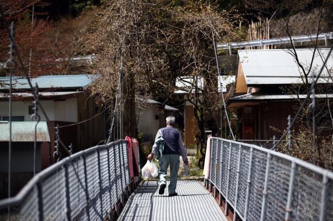 © Bloomberg. MIYOSHI, JAPAN - APRIL 22: An elderly man crosses a bridge to his home in a small village, on April 22, 2016 in Miyoshi, Japan. Many rural areas of Japan have become heavily depopulated as younger people leave for cities and larger towns in search of work and better prospects. Many of the people who remain are pensioners who, according to Japan's Statistic Bureau, make up 26.8 percent of the population compared to the 8.2 percent average for the rest of the world. (Photo by Carl Court/Getty Images)