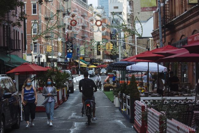 © Bloomberg. People wearing protective masks walk down a street lined with outdoor seating for restaurants in the Little Italy neighborhood of New York on July 6. Photographer: Angus Mordant/Bloomberg