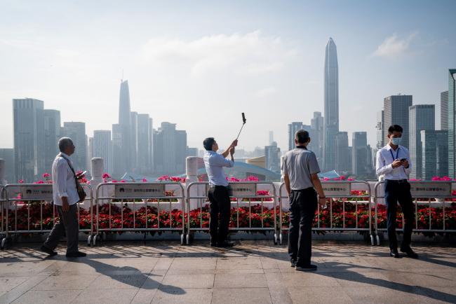 © Bloomberg. People take photographs against a backdrop of the Shenzhen skyline at Lianhuashan Park in Shenzhen, China, on Friday, Nov. 20, 2020. China will likely return to a more 