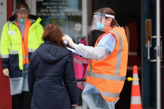 © Bloomberg. CHRISTCHURCH, NEW ZEALAND - MARCH 24: Staff wearing personal protective equipment check the temperature of patients in front of a medical centre on March 24, 2020 in Christchurch, New Zealand. Prime Minister Jacinda Ardern has lifted New Zealand's COVID-19 alert level to three on Monday, and will raise the alert level to four on Wednesday as the government works to stop the spread of COVID-19. With community transmission now a possibility in New Zealand, the Prime Minister has said staying at home is essential. Schools are now closed and all non-essential businesses including bars, restaurants, cinemas, playgrounds will close Wednesday. All indoor and outdoor events are banned. Essential services will remain open. New Zealand currently has 155 confirmed cases of COVID-19. (Photo by Kai Schwoerer/Getty Images)