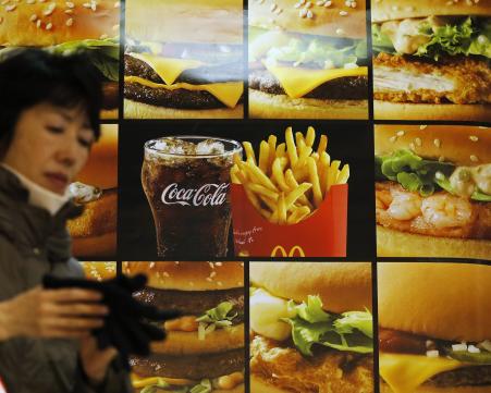 © Reuters. A woman walks past an advertisement showing McDonald's burgers, fries and a drink, outside a McDonald's store in Tokyo. Japan's McDonald's experienced its second crisis in two months as a a piece of vinyl was found in its McNuggets this week.