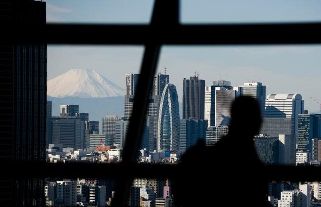 © Bloomberg. Mount Fuji stands beyond buildings as a visitor looks out at the skyline from an observation deck in Tokyo, Japan, on Friday, Jan. 11, 2019. Japan’s key inflation gauge slowed in the first back-to-back decline since April, highlighting the difficulty of the Bank of Japan’s price goal ahead of its policy meeting next week. Photographer: Akio Kon/Bloomberg