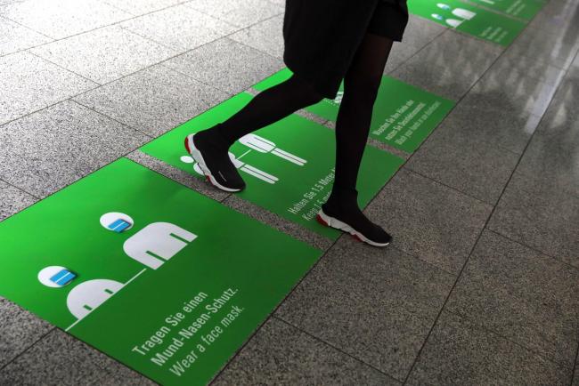 © Bloomberg. A traveler walks over social distancing and protective face mask information floor signs at Frankfurt Airport, operated by Fraport AG, in Frankfurt, Germany, on Tuesday, May 12, 2020. The Covid-19 crisis has brought global air travel almost to a halt, with governments closing borders and urging populations to stay at home to contain the pandemic. Photographer: Alex Kraus/Bloomberg