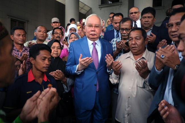 © Bloomberg. Najib Razak, Malaysia's former prime minister, center, offers prayers with his supporters as he arrives at the Kuala Lumpur Courts Complex in Kuala Lumpur, Malaysia, on Tuesday, Dec. 3, 2019. Najib is set to give his testimony to defend himself against charges of corruption involving a former 1MDB unit. Photographer: Samsul Said/Bloomberg