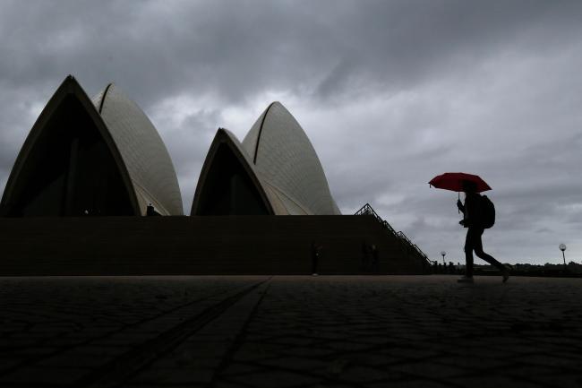 © Bloomberg. A pedestrian holding an umbrella walks past the closed Sydney Opera House stands in Sydney, Australia, on Tuesday, March 24, 2020. Australia's parliament rushed through more than A$80 billion ($46.3 billion) in fiscal stimulus for the coronavirus-stricken economy at a special sitting in Canberra on March 23. Photographer: Brendon Thorne/Bloomberg