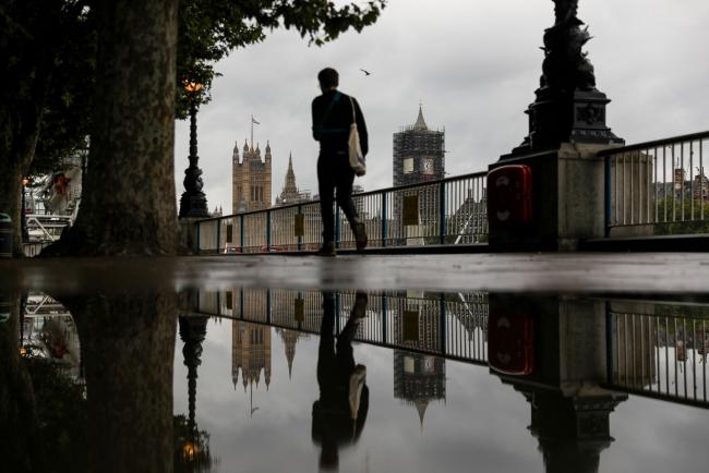 © Bloomberg. A pedestrian passes a puddle reflecting the Houses of Parliament in London on Aug. 27. Photographer: Simon Dawson/Bloomberg