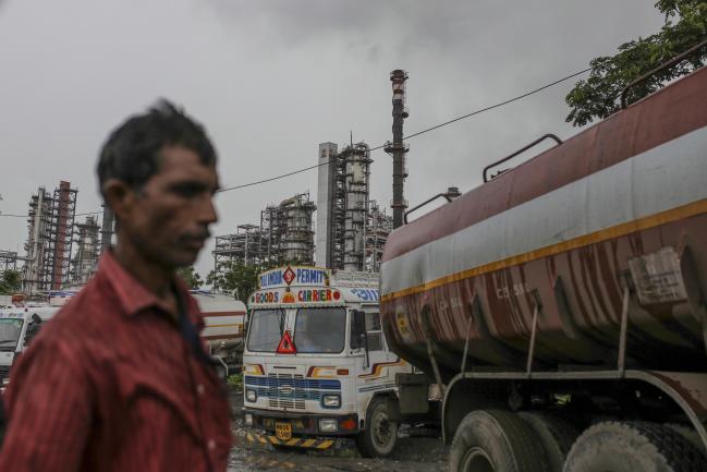© Bloomberg. A pedestrian walks past trucks parked in front of the Bharat Petroleum Corp. refinery in the Mahul area of Mumbai, India, on Thursday, June 28, 2018. The Indian rupee slumped to an all-time low as a resurgence in crude prices and the emerging-market selloff took a toll on the currency of the world's third-biggest oil consumer. Photographer: Dhiraj Singh/Bloomberg