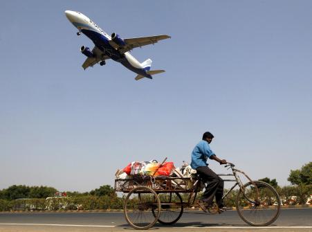 © Reuters/Amit Dave. An IndiGo airlines aircraft prepares to land as a man rides his cycle rickshaw in Ahmedabad, India, Oct. 26, 2015.